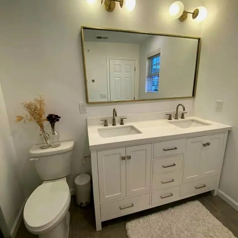 Renovated bathroom with a white double vanity, a brass-framed mirror and brass wall sconces.