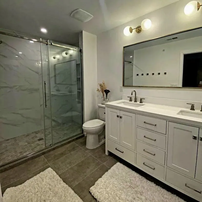 Renovated bathroom with a white double vanity, a wide mirror, brass wall sconces and a glass shower enclosure.