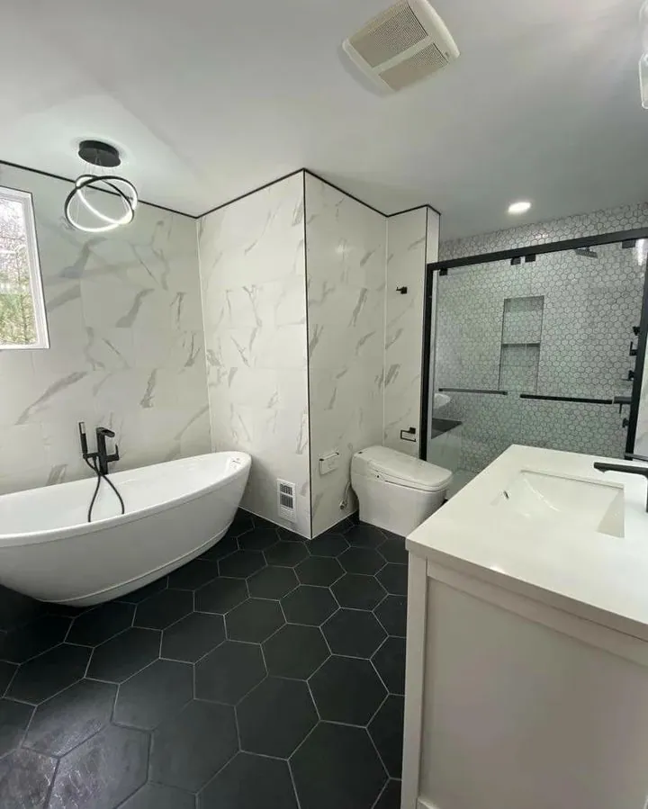 Renovated bathroom with a freestanding oval tub, marble-look wall tile, a white vanity and dark hexagon floor tile.