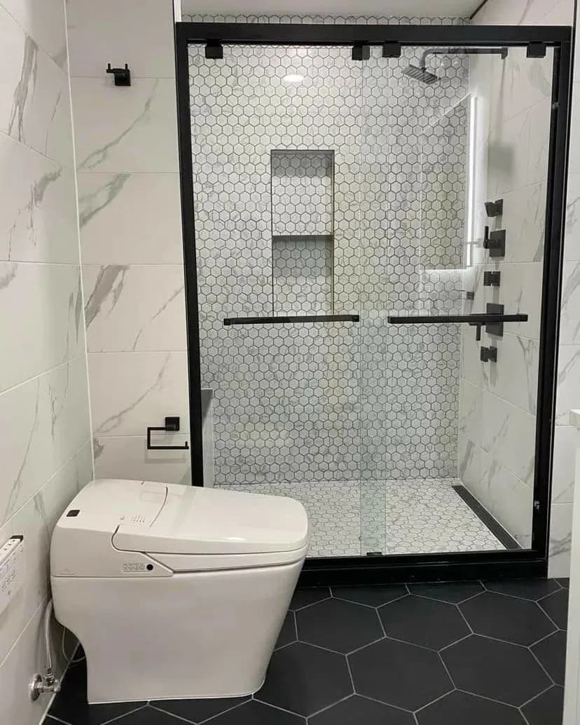 Renovated bathroom with a glass shower enclosure, marble-look wall tile and hexagon floor tile.