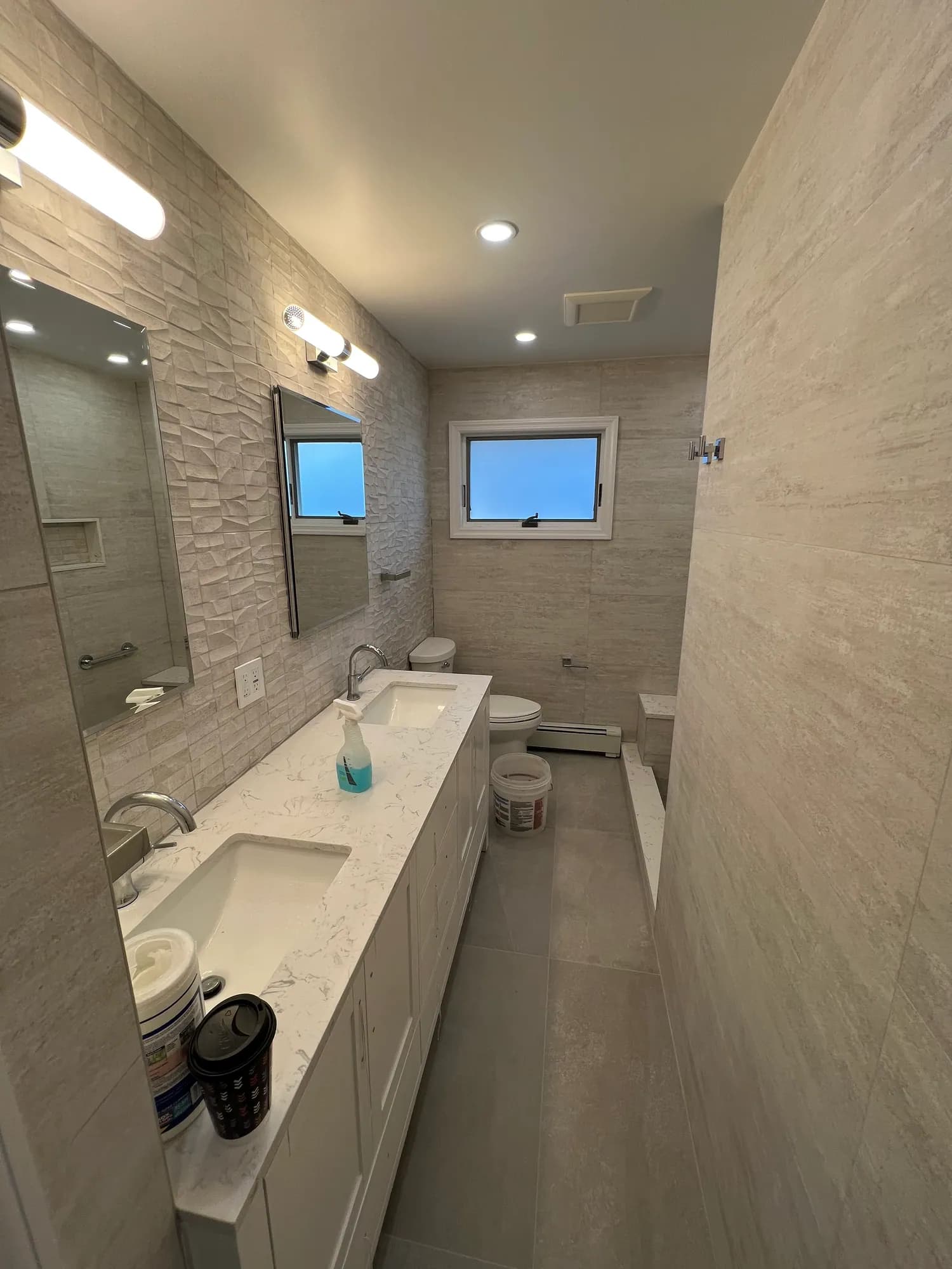 Renovated bathroom with a white double vanity, two mirrors, wall sconces and large-format grey wall tile.