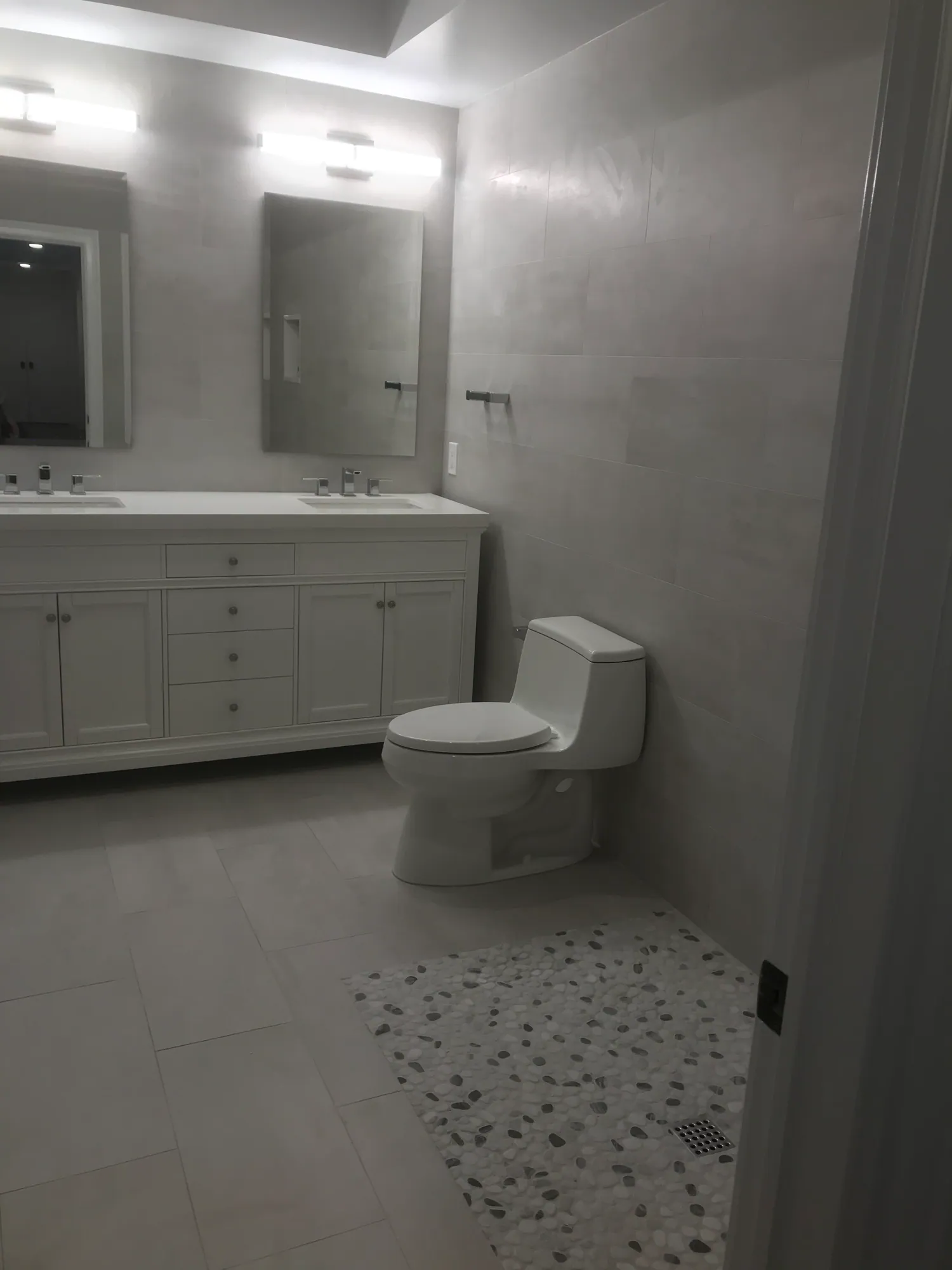 Renovated bathroom with a grey double vanity, a wide mirror, grey wall tile and pebble-pattern floor tile.