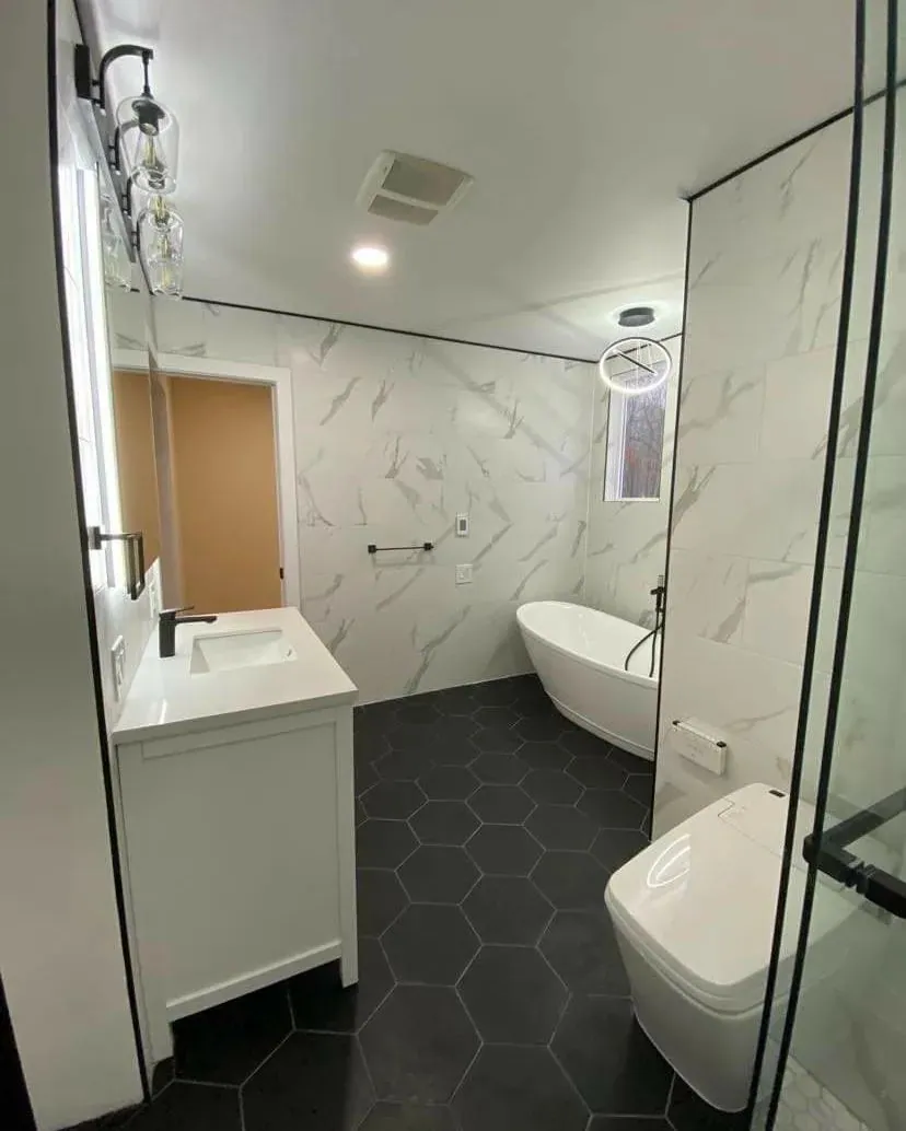 Renovated bathroom with marble-look wall tile, a freestanding tub, a glass shower panel and dark hexagon floor tile.