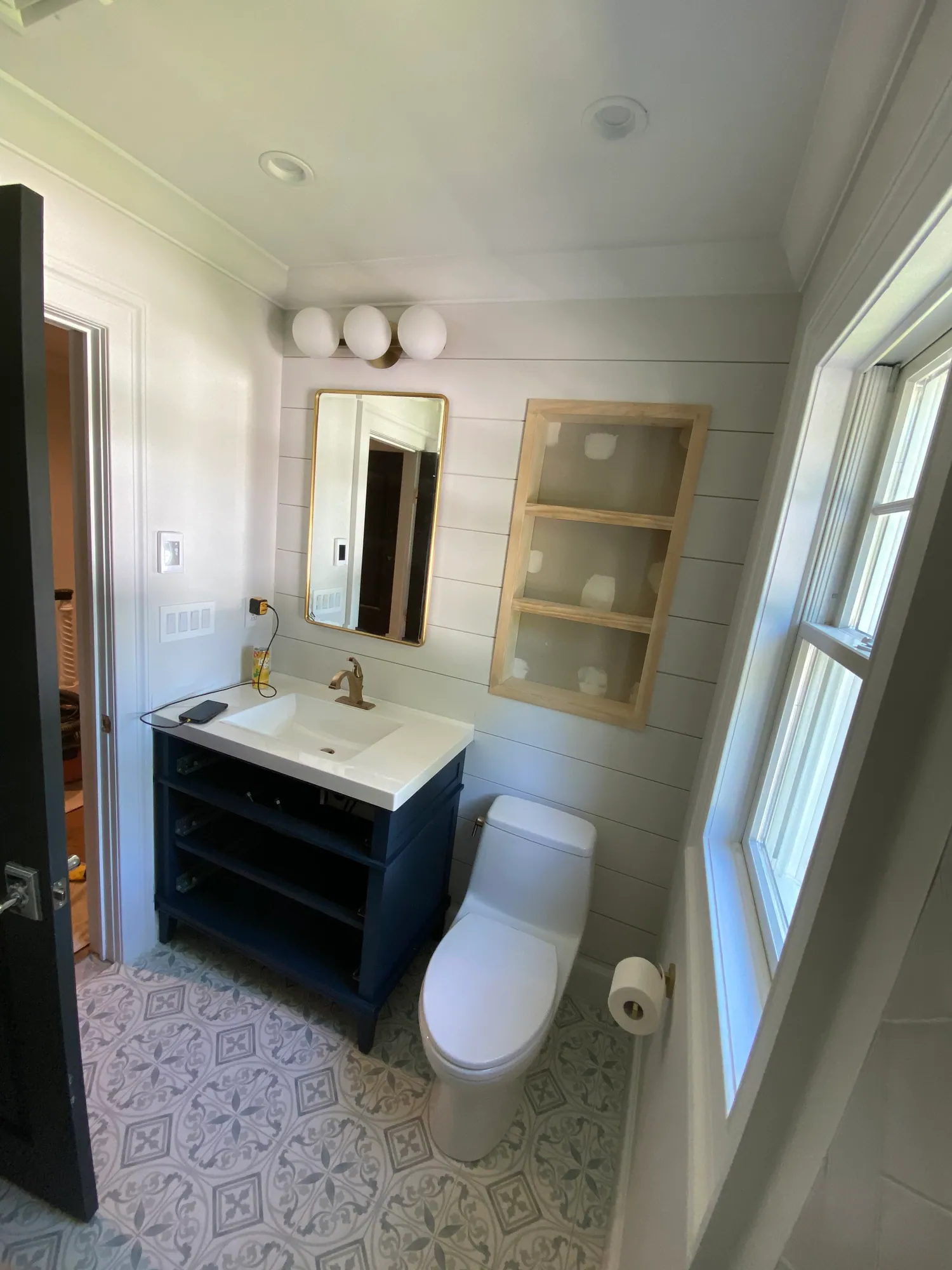 Renovated bathroom with a navy vanity, white shiplap walls, a black-framed mirror and patterned floor tile.