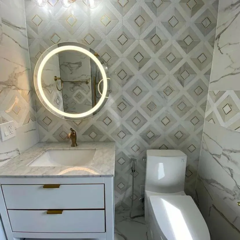 Renovated bathroom with a white vanity, marble-look countertop, a round backlit mirror and a geometric patterned feature wall.