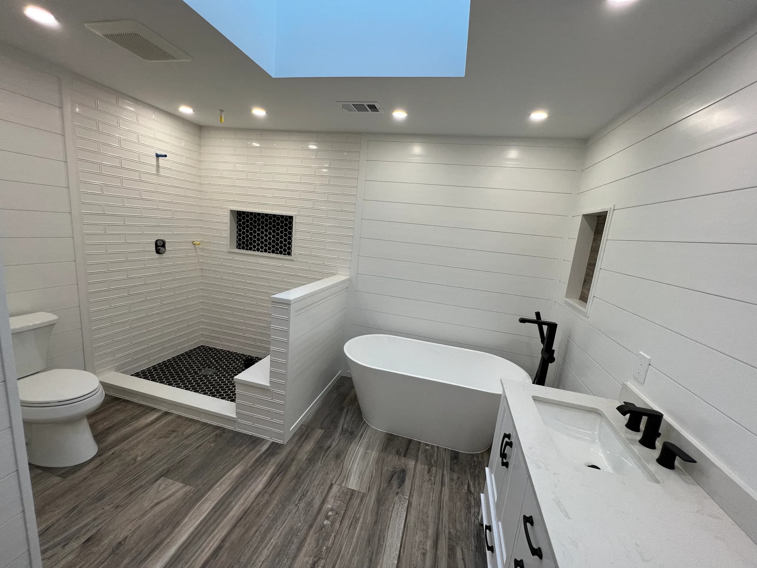 Renovated bathroom with a freestanding tub, a tiled walk-in shower with a built-in bench, white shiplap walls and a skylight above.
