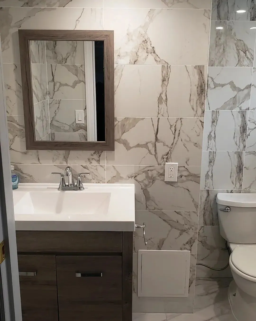 Renovated bathroom with a white vanity, marble-look wall tile and a wood-framed mirror.