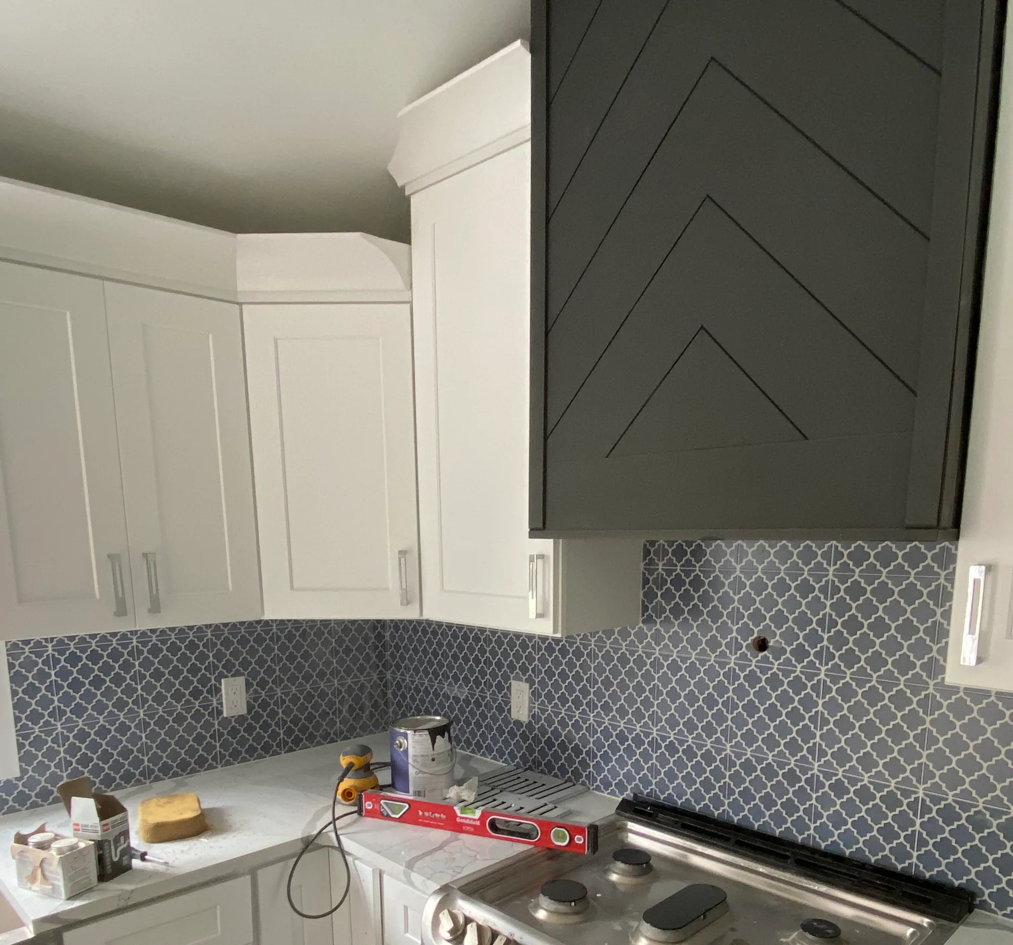 Kitchen wall with white shaker cabinets, a dark chevron range hood and a blue arabesque tile backsplash.