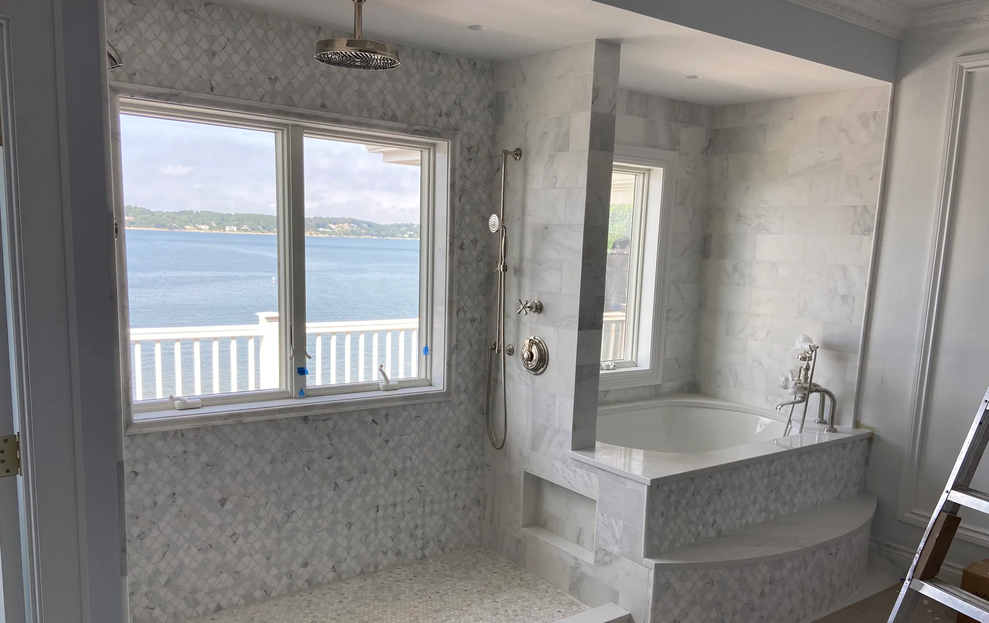 Bathroom under construction with marble mosaic tile on the walls and a tiled tub deck beneath a window.