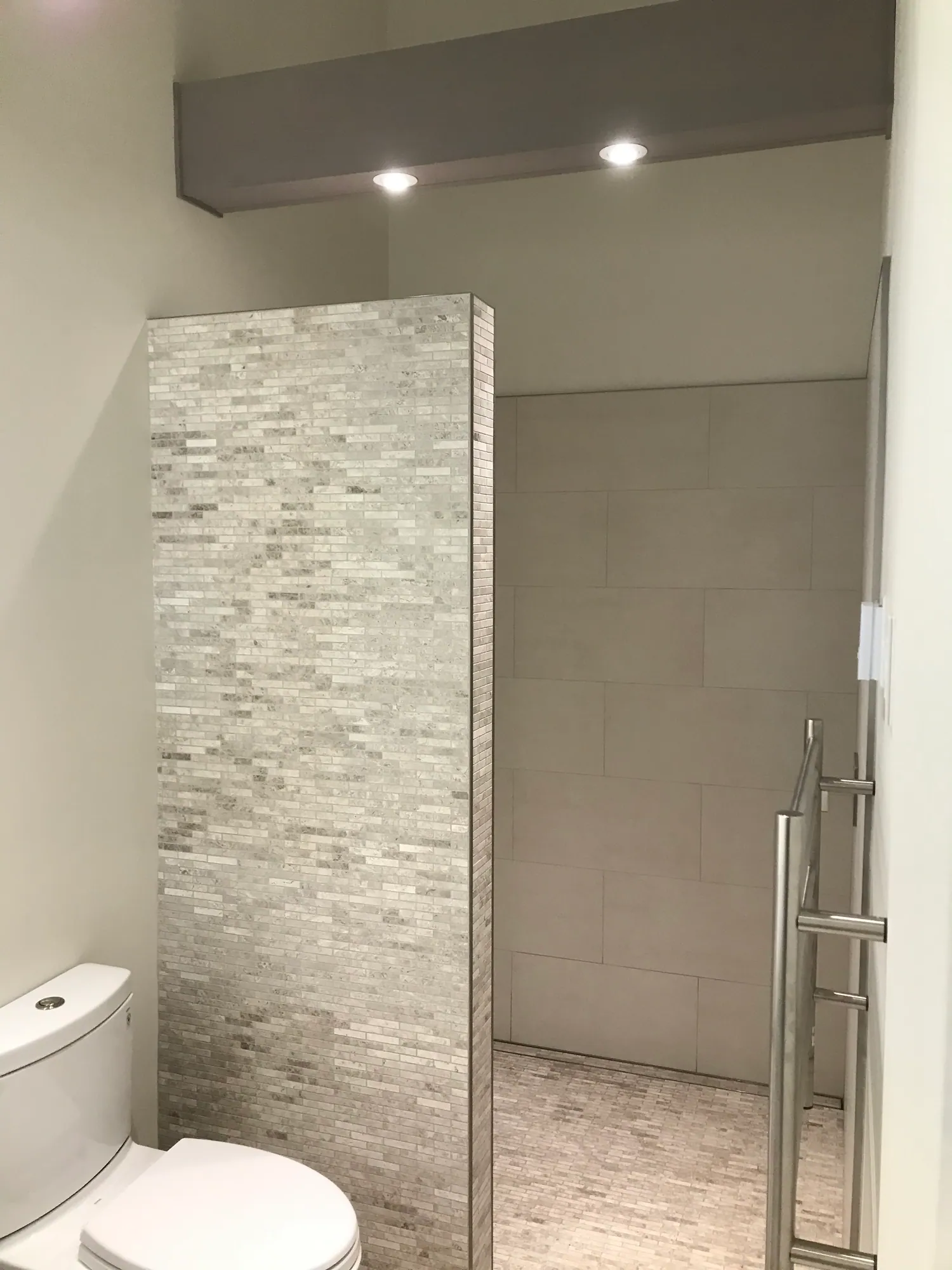 Close view of a stacked stone accent wall meeting large-format tile inside a shower.