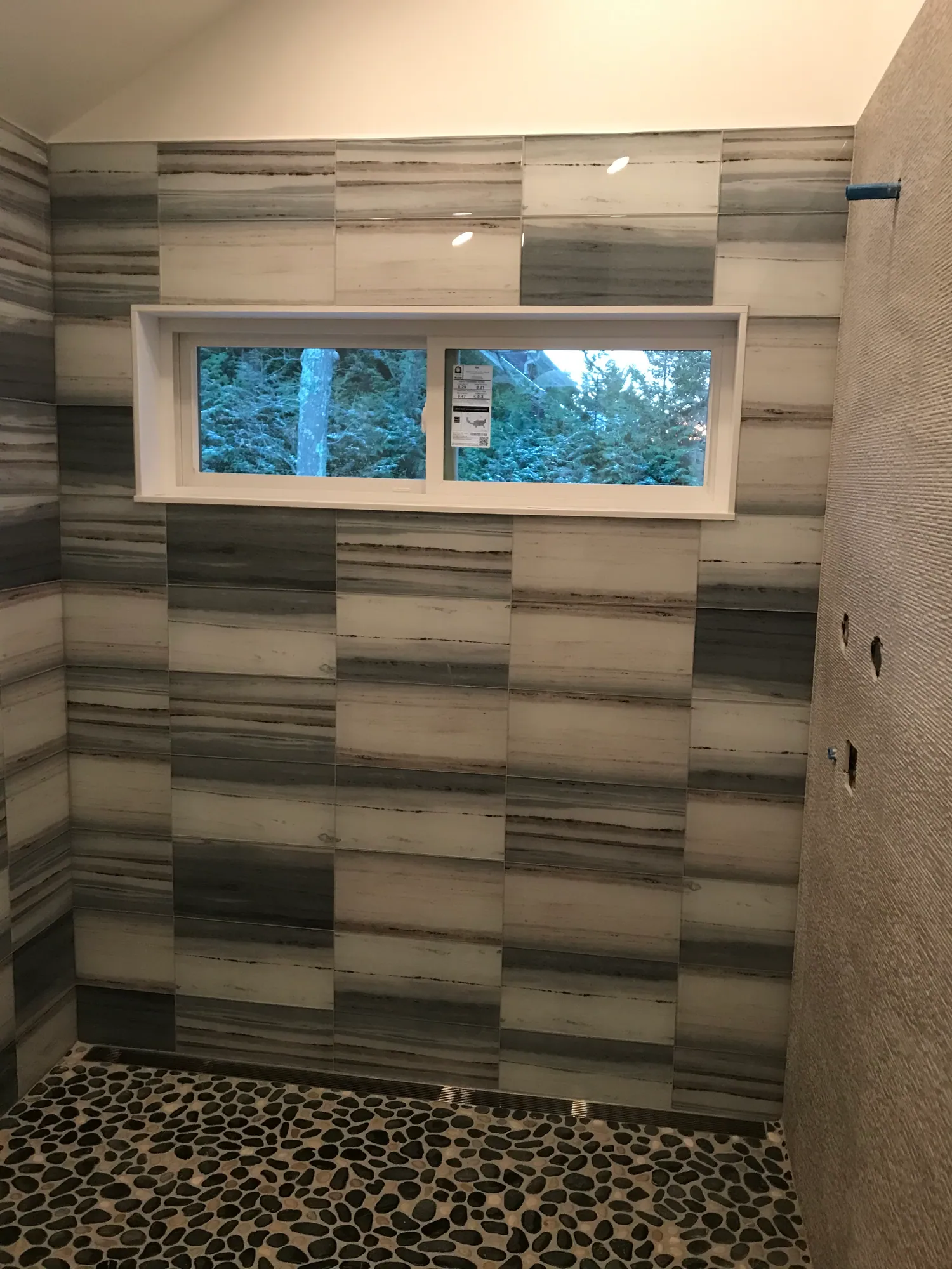 Close view of grey striated stone-look tile running across a shower wall and around a window opening.