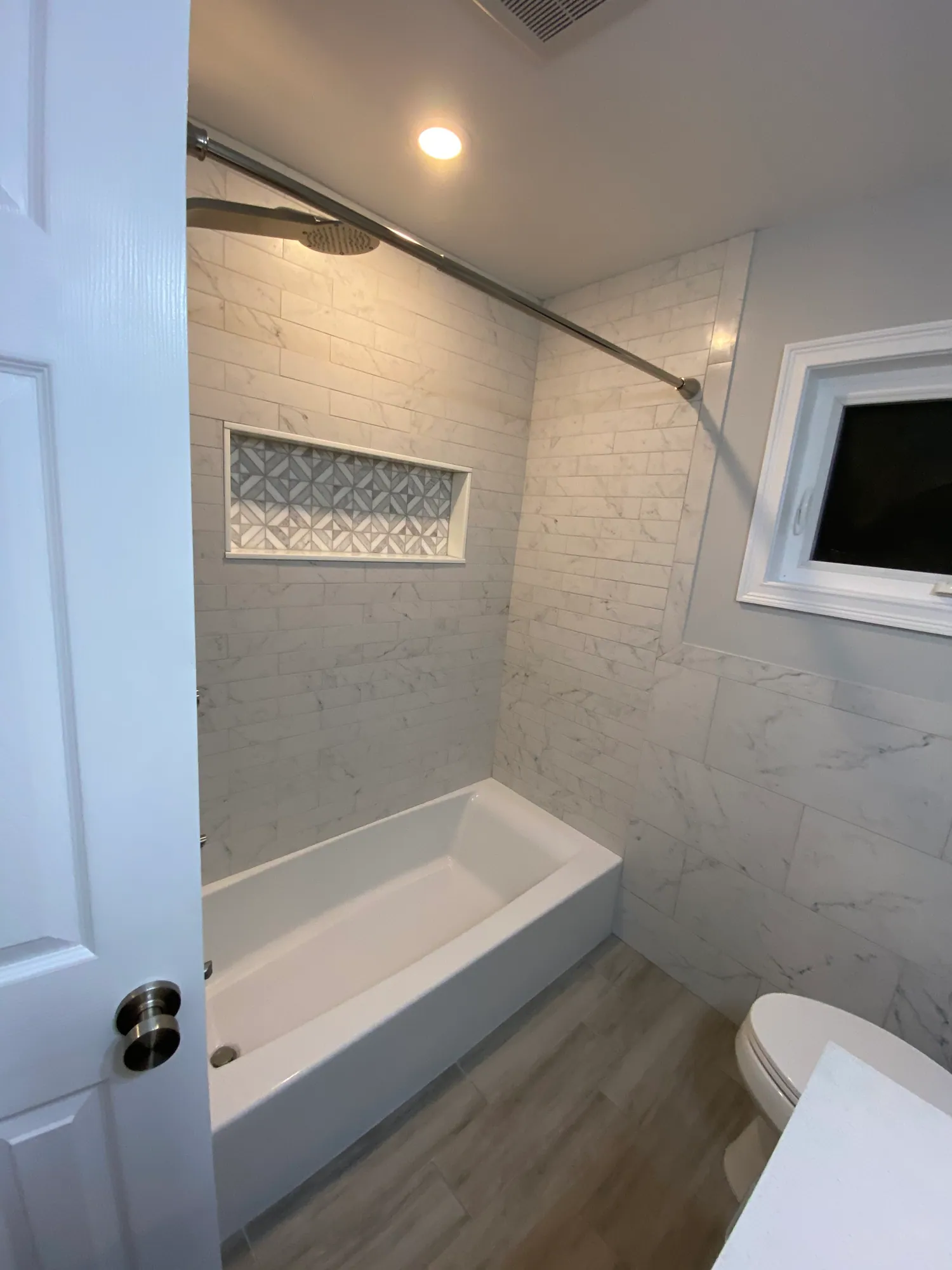 Tub surround in marble-look tile with a long decorative patterned niche above it.