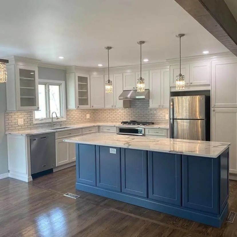 Renovated kitchen with white shaker cabinets, a navy island with a marble-look countertop, brick-pattern backsplash and glass pendant lights.