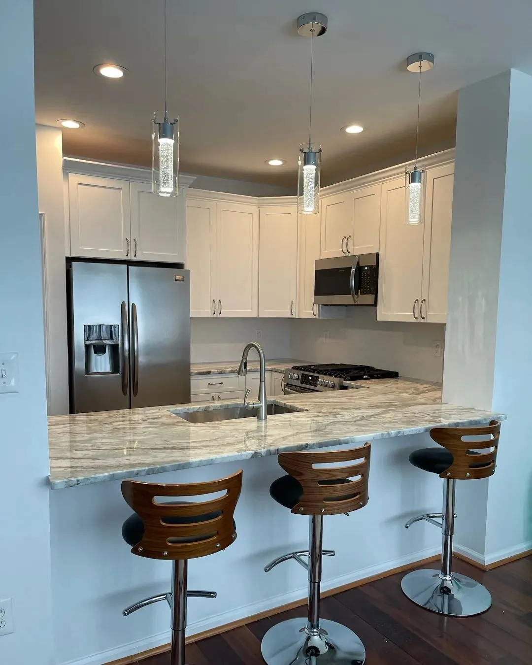 Renovated kitchen with white cabinets, a raised breakfast peninsula with bar stools and glass pendant lighting.