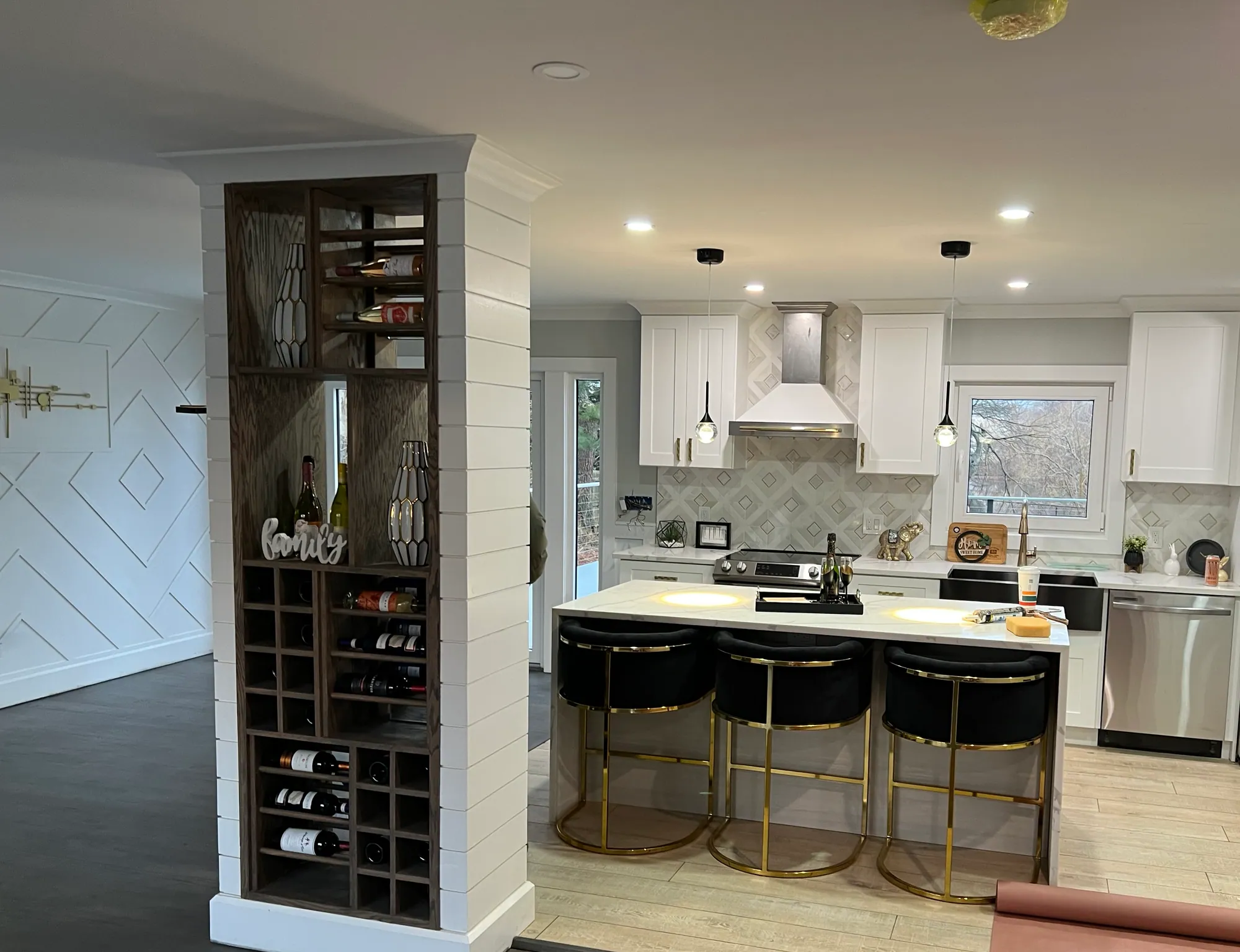 Open kitchen renovation with white cabinets, a built-in wine rack column, a range hood and an island with upholstered bar stools.