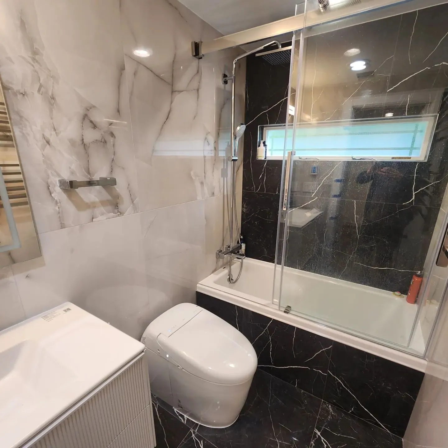 Shower with white and black marble-look tile, a glass enclosure, a wall niche and a built-in tub surround.