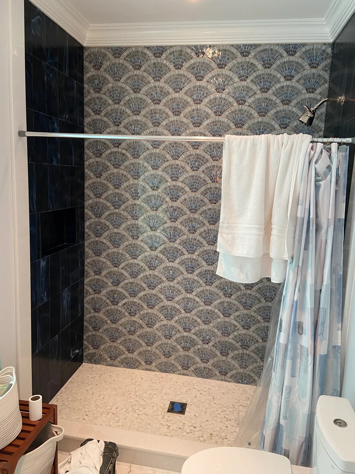 Walk-in shower with blue fish-scale mosaic wall tile, a black tile border and a speckled terrazzo-look floor.