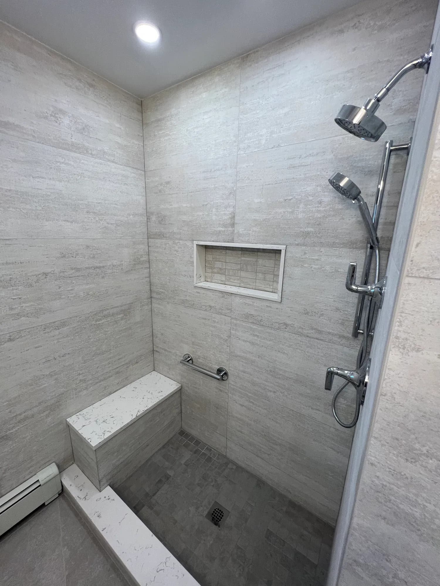 Walk-in shower with large-format grey wall tile, a built-in bench, a wall niche and a rain shower head.