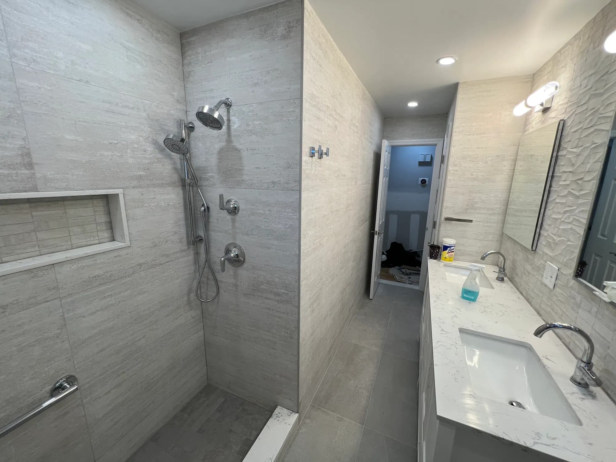 Walk-in shower with large-format grey tile and a glass panel, next to a white vanity.