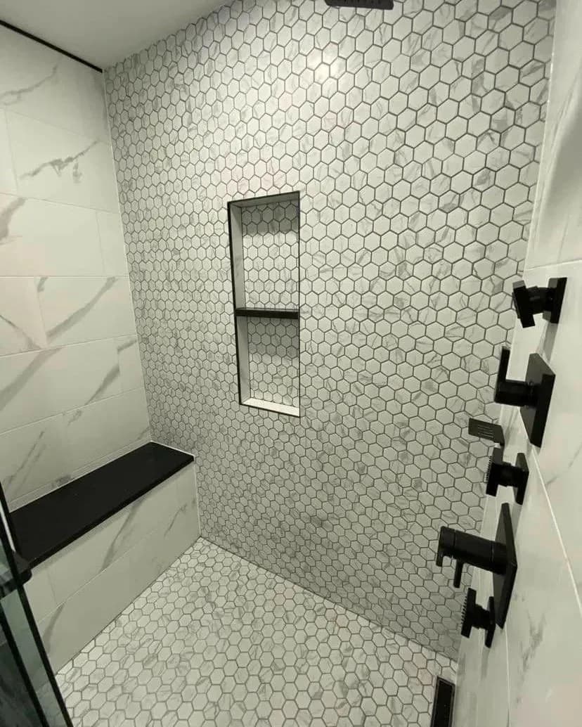 Walk-in shower with white hexagon mosaic wall tile, a built-in niche, a stone bench and matte black fixtures.