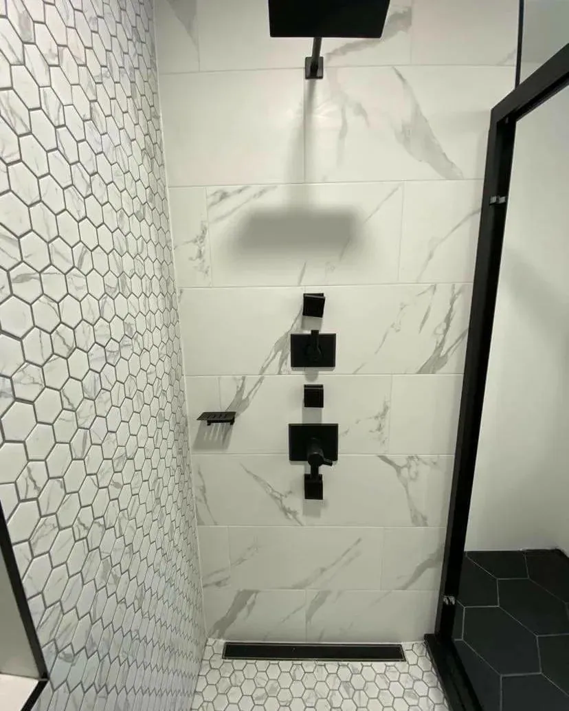 Walk-in shower with marble-look wall tile, a rain shower head, matte black fixtures and hexagon mosaic tile.