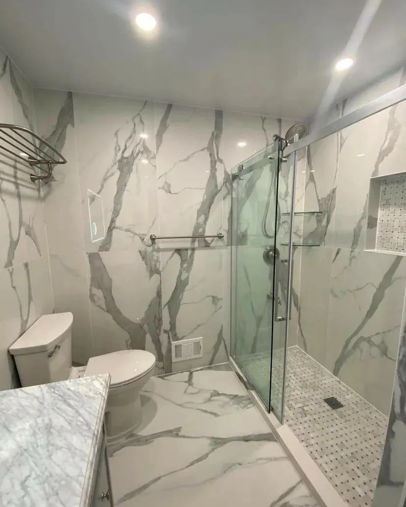 Walk-in shower with large marble-look wall tile, a frameless glass enclosure and hexagon mosaic floor tile.
