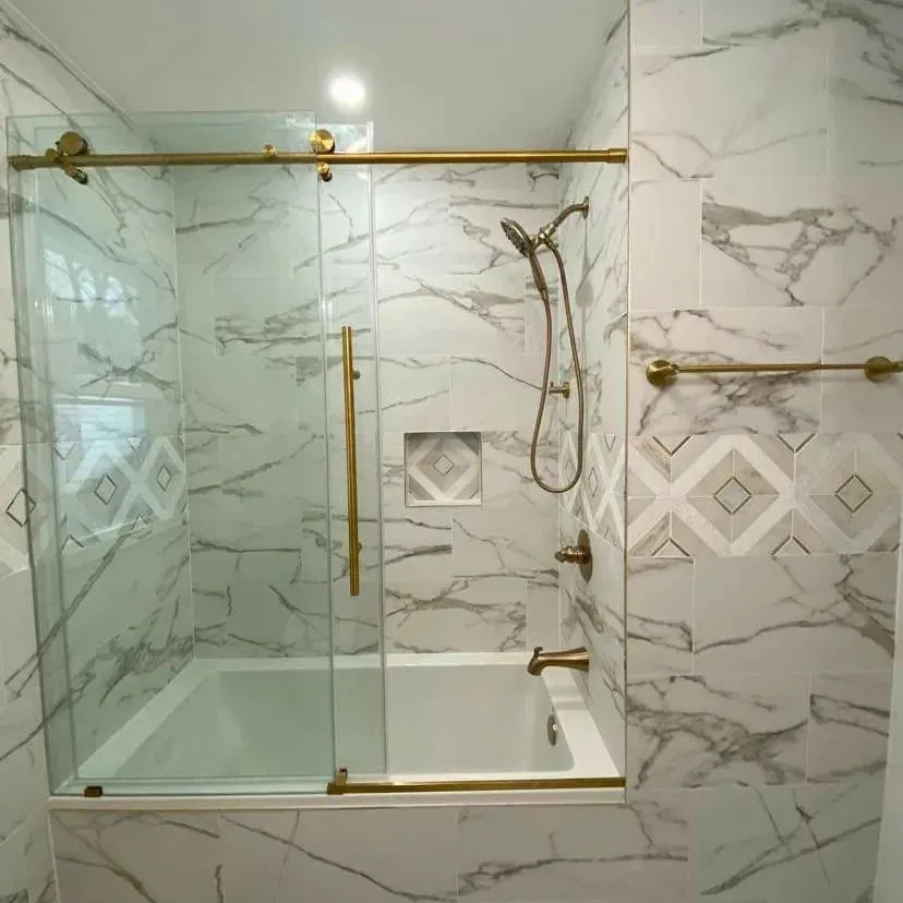 Tub and shower lined in marble-look tile with a decorative diamond tile band, brass fixtures and a sliding glass door.