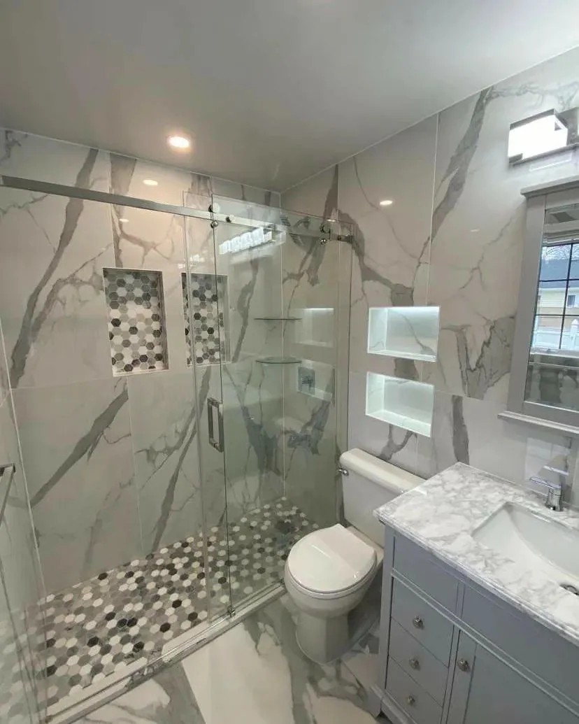 Walk-in shower with marble-look wall tile, two mosaic-lined niches and a frameless glass enclosure.