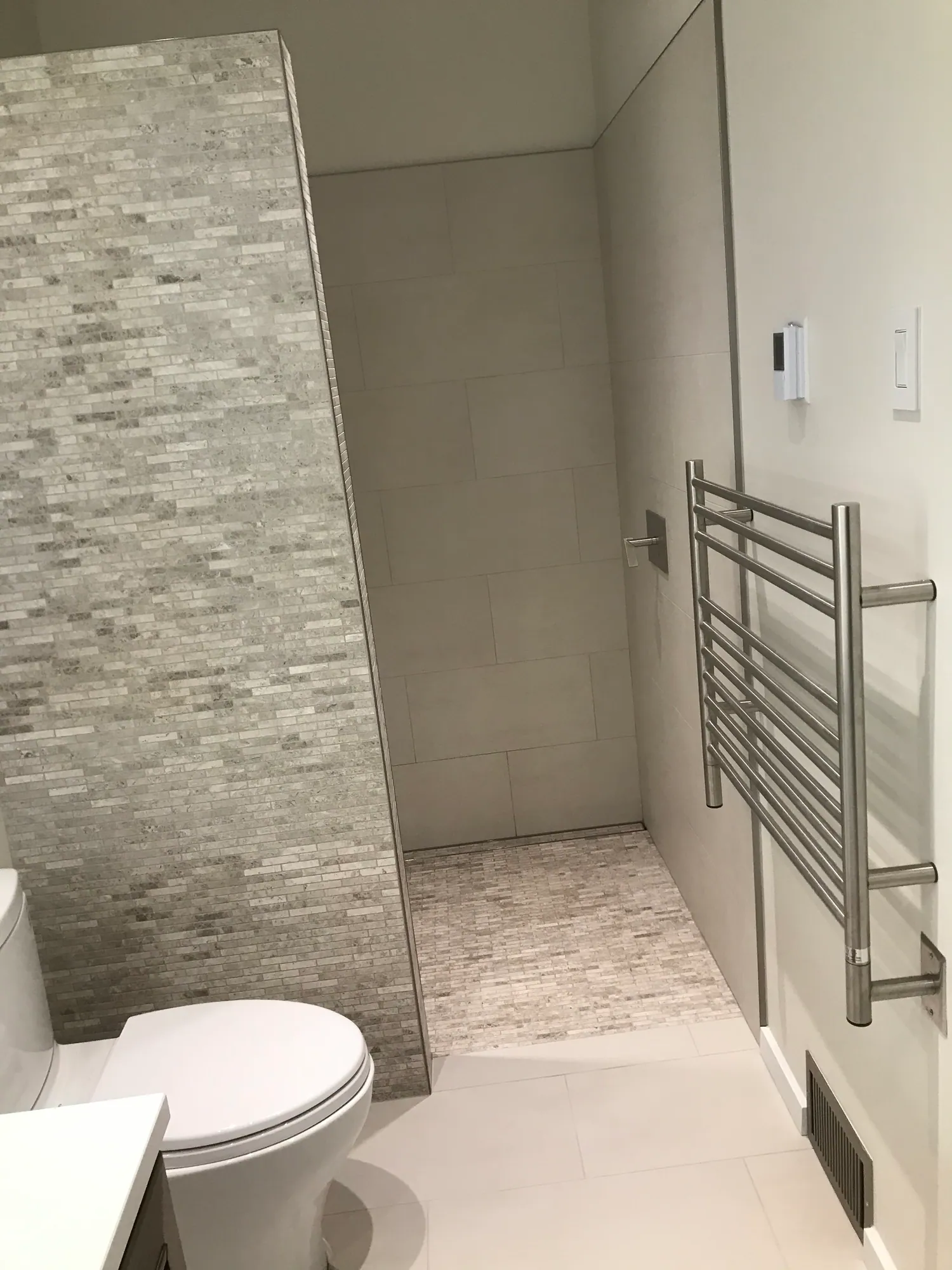 Walk-in shower with a stacked stone accent wall, large-format tile and a wall-mounted towel warmer.