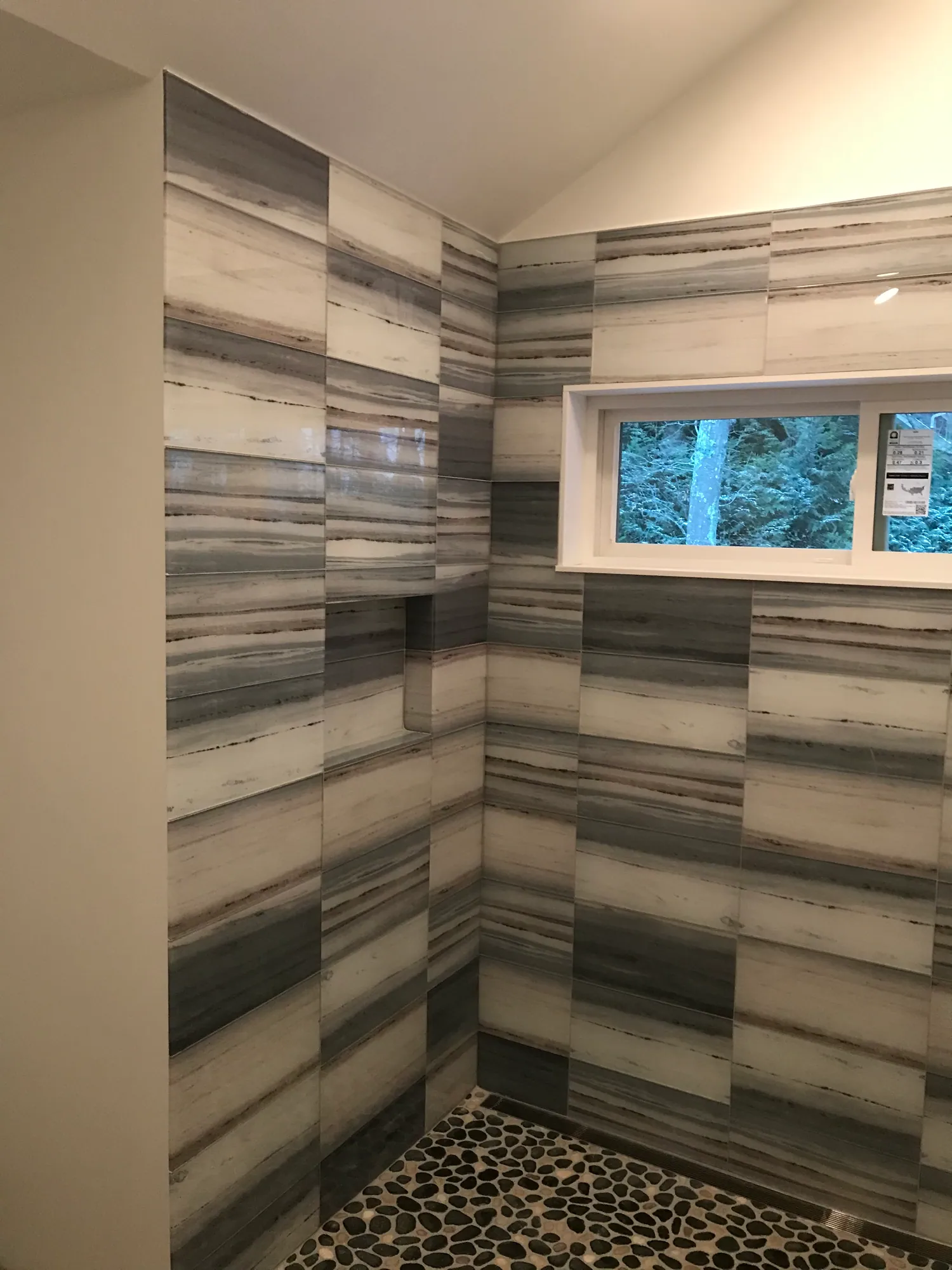 Walk-in shower lined in grey striated stone-look tile with a pebble floor and a glass panel.