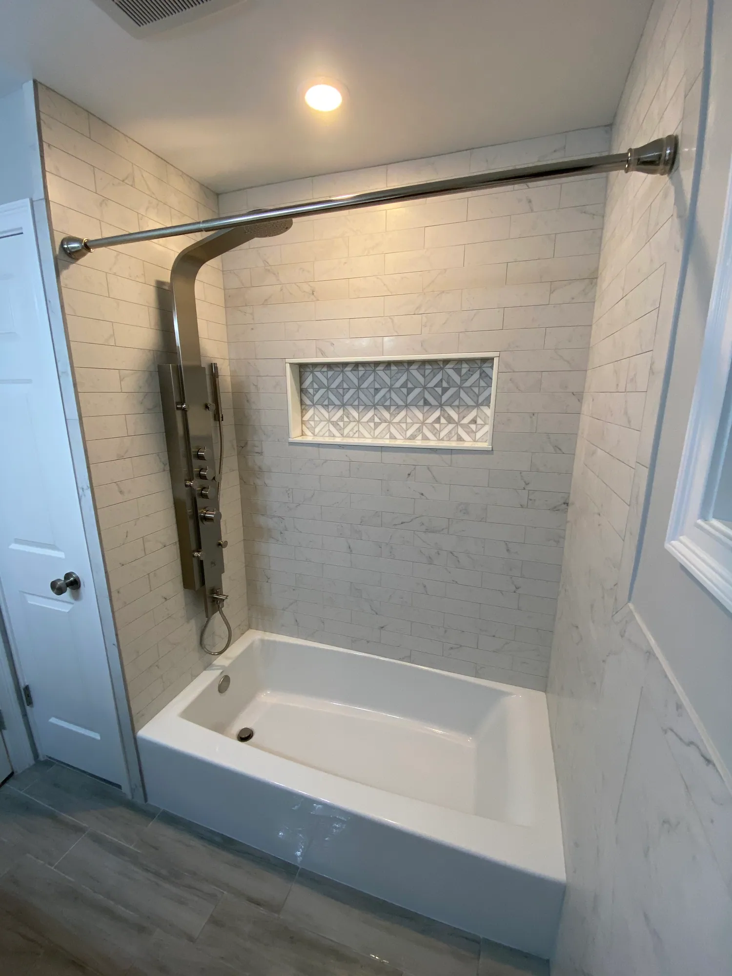 Tub and shower surround in marble-look tile with a decorative patterned niche and a wall-mounted shower fitting.