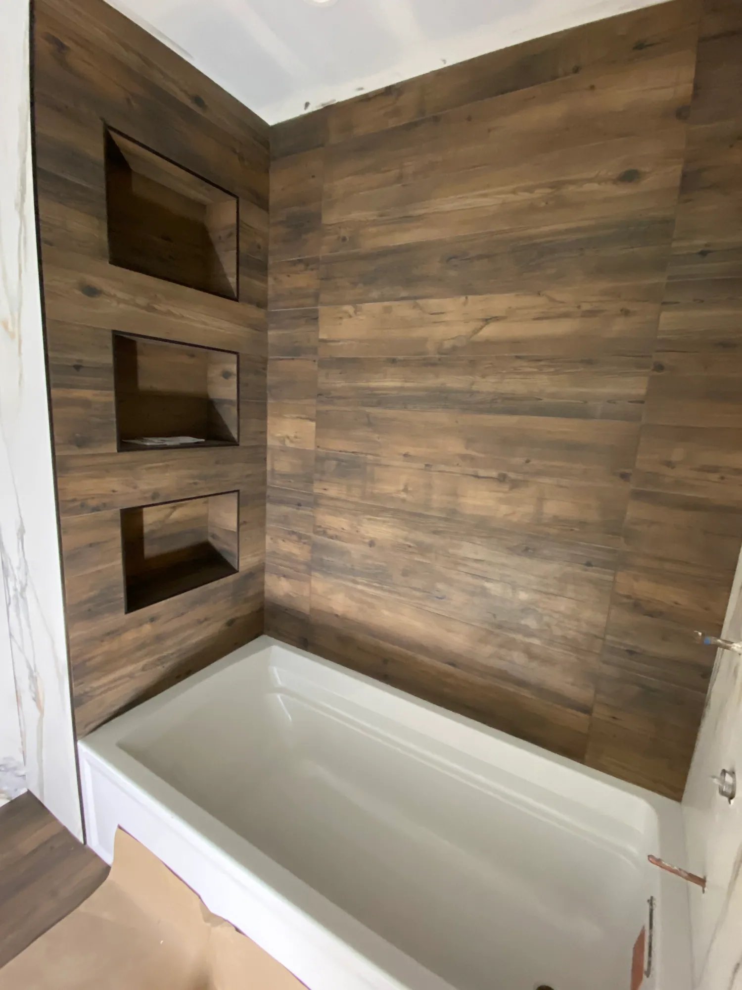 Tub and shower surround in wood-look tile with a column of stacked built-in niches.